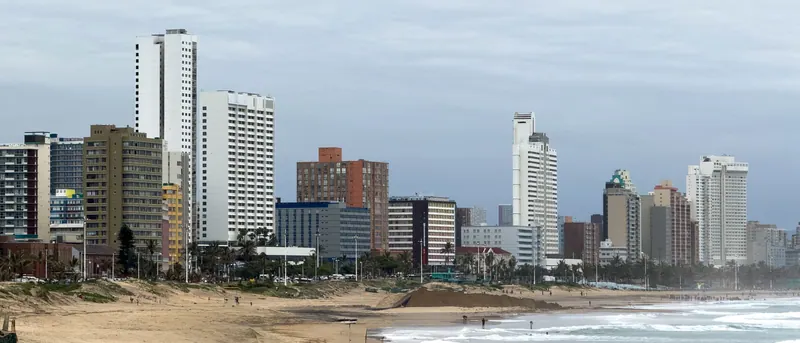 Durban's beachfront towers seen across the sand and surf under an overcast sky.