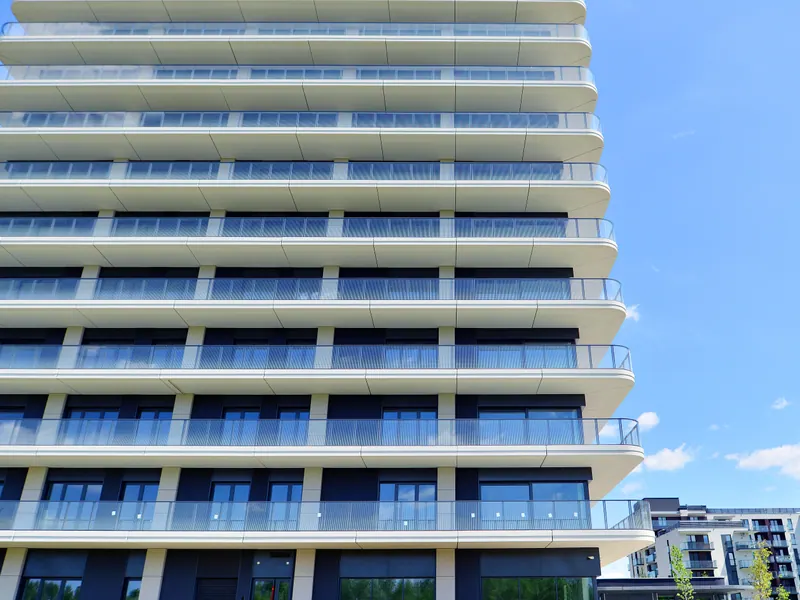A white high-rise apartment building with deep balconies on every floor under a blue sky.